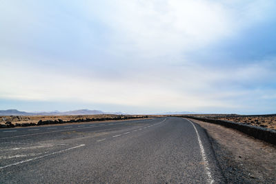 Empty road passing through landscape against cloudy sky