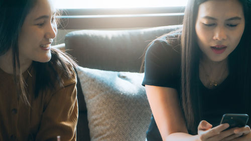 Woman using mobile phone while sitting with friend at home