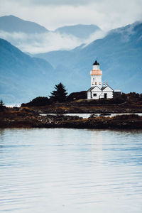 Lighthouse by lake and buildings against sky