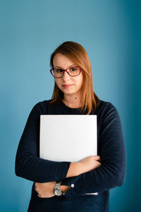 Portrait of beautiful young woman standing against blue background