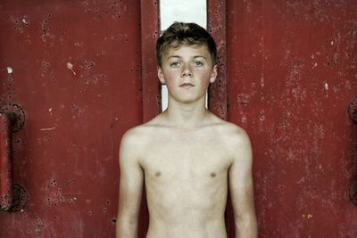 Portrait of shirtless teenage boy standing against red gate