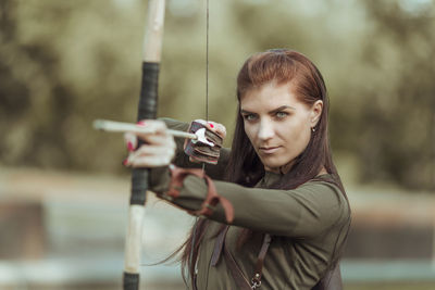Beautiful archer holding bow and arrow standing against blurred background