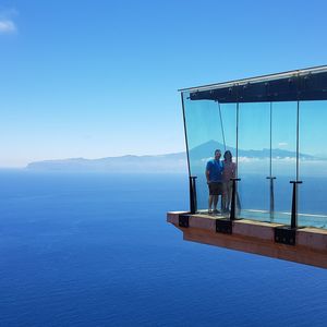 People standing at sea shore against clear blue sky