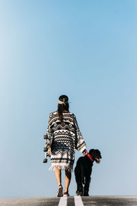 Rear view of woman with dog against clear sky