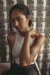 Portrait of young woman sitting against wall