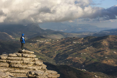 Side view of woman looking at landscape while standing on mountain against cloudy sky