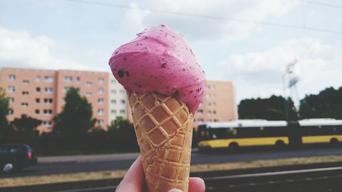 Close-up of hand holding ice cream cone against sky