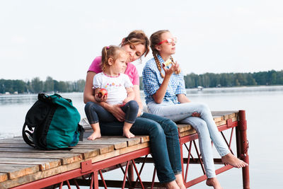 Mother with daughters sitting on pier over lake