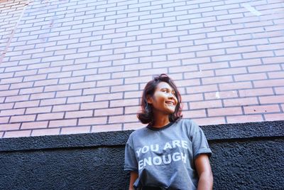 Low angle view of young woman smiling while standing by wall