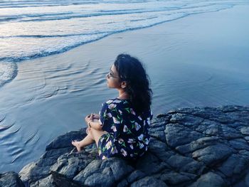 High angle view of woman sitting on rock by sea