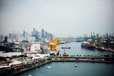 Boats in harbor by buildings in city against sky