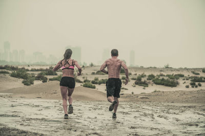 Rear view of shirtless man running on beach