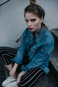 High angle portrait of young woman sitting against wall