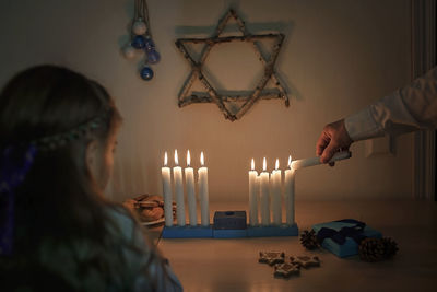 Cropped hand of mother lighting candles with cute girl at home