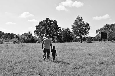 Rear view of father walking with son on grassy field