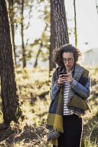 Woman using phone while standing in forest