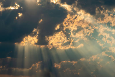 Low angle view of sunlight streaming through clouds