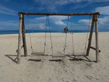 Empty swings at beach against blue sky