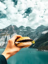 Midsection of person holding ice cream against mountains