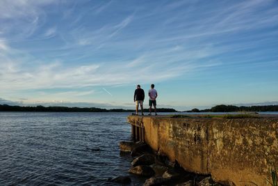 Men standing on retaining wall by lake against sky