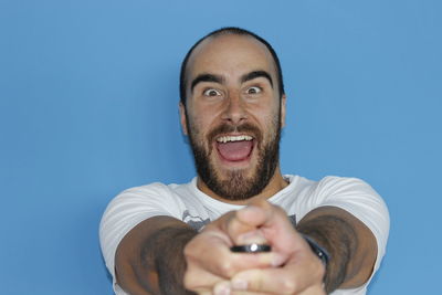 Portrait of excited man pressing button while standing against blue background