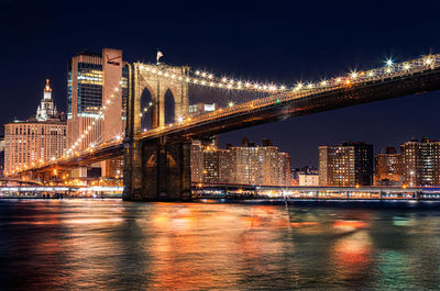 Illuminated bridge over river in city at night