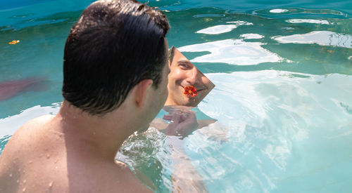 Reflection of man holding flower in mirror while sitting in swimming pool