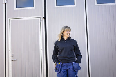 Female blue-collar worker with hands in pockets standing against door