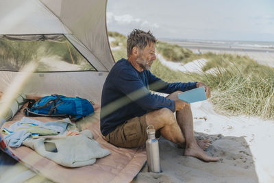 Mature man reading book at beach on sunny day