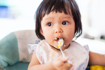 Close-up of baby girl eating food on high chair at home