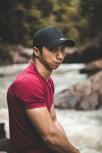 Portrait of young man sitting by river at forest