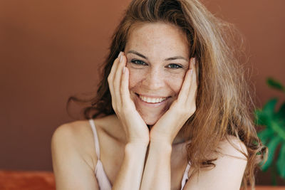 Laughing red-haired freckled woman touches her face with her hands and looks at the camera.