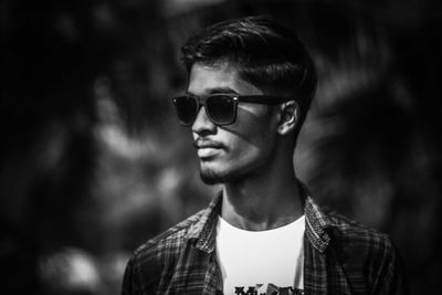 Young man wearing sunglasses looking away while standing outdoors