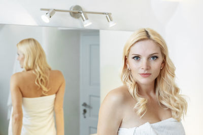 Blond woman in a white bathroom looking at the camera, wearing a towel