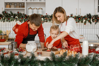 Family in the kitchen are busy cutting raw dough with a cookie cutter on the table. christmas time.