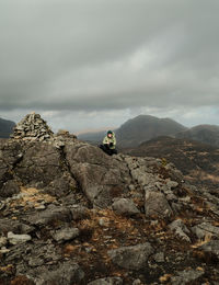 Rear view of man sitting on rock against sky