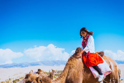 Woman riding camel in desert against sky