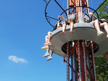 Low angle view of people sitting on amusement park ride against blue sky during sunny day