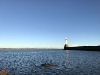 Lighthouse by sea against clear blue sky