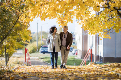 A mature couple holding hands goes for a walk in an autumn park from a residential area