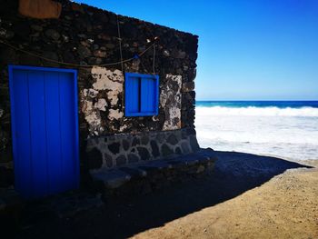 Built structure on beach by building against blue sky