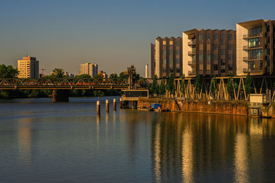 Bridge over river by buildings against clear sky