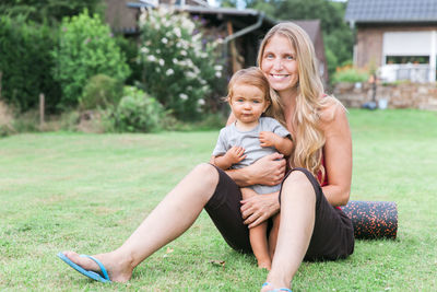 Portrait of happy mother and daughter sitting on grass