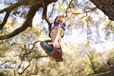 Low angle view of girl playing on rope swing in forest