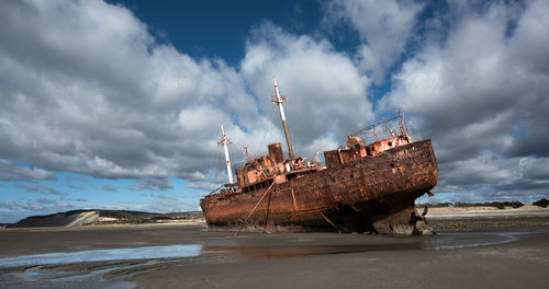 Panoramic view of abandoned ship on beach against sky
