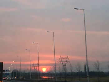 Silhouette street lights against orange sky at sunset