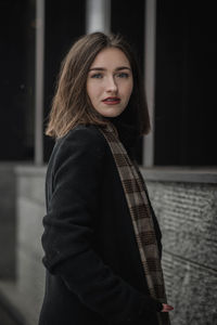 Portrait of young woman in warm clothing standing against building