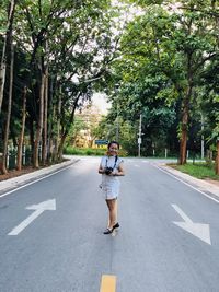 Woman standing on road amidst trees