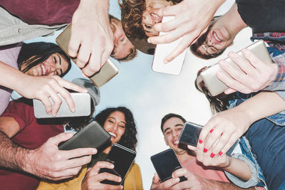 Low angle view of friends using mobile phones while standing against sky