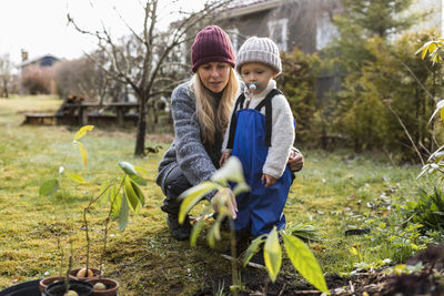 Mid adult woman with son wearing knit hat looking at plants in backyard